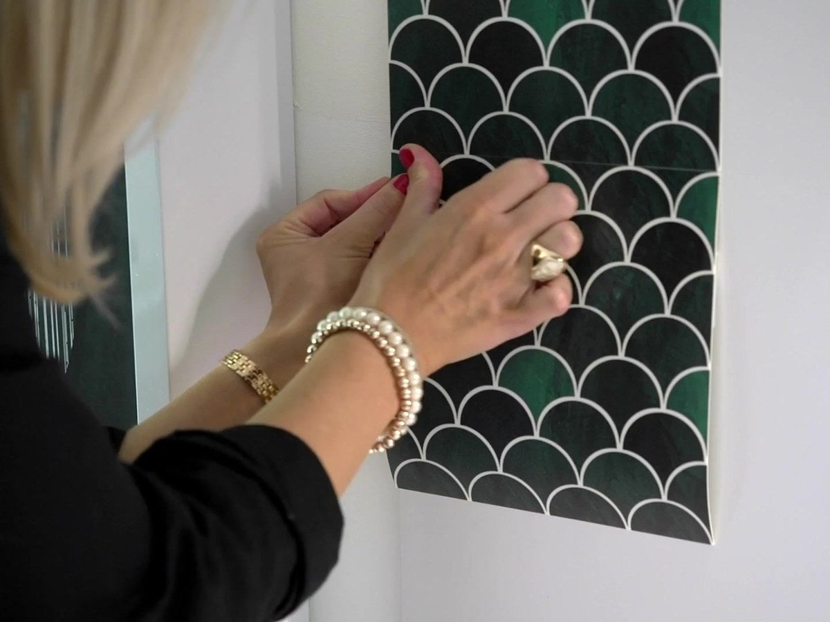 Mains posant un carreau adhésif effet écaille sur un mur blanc